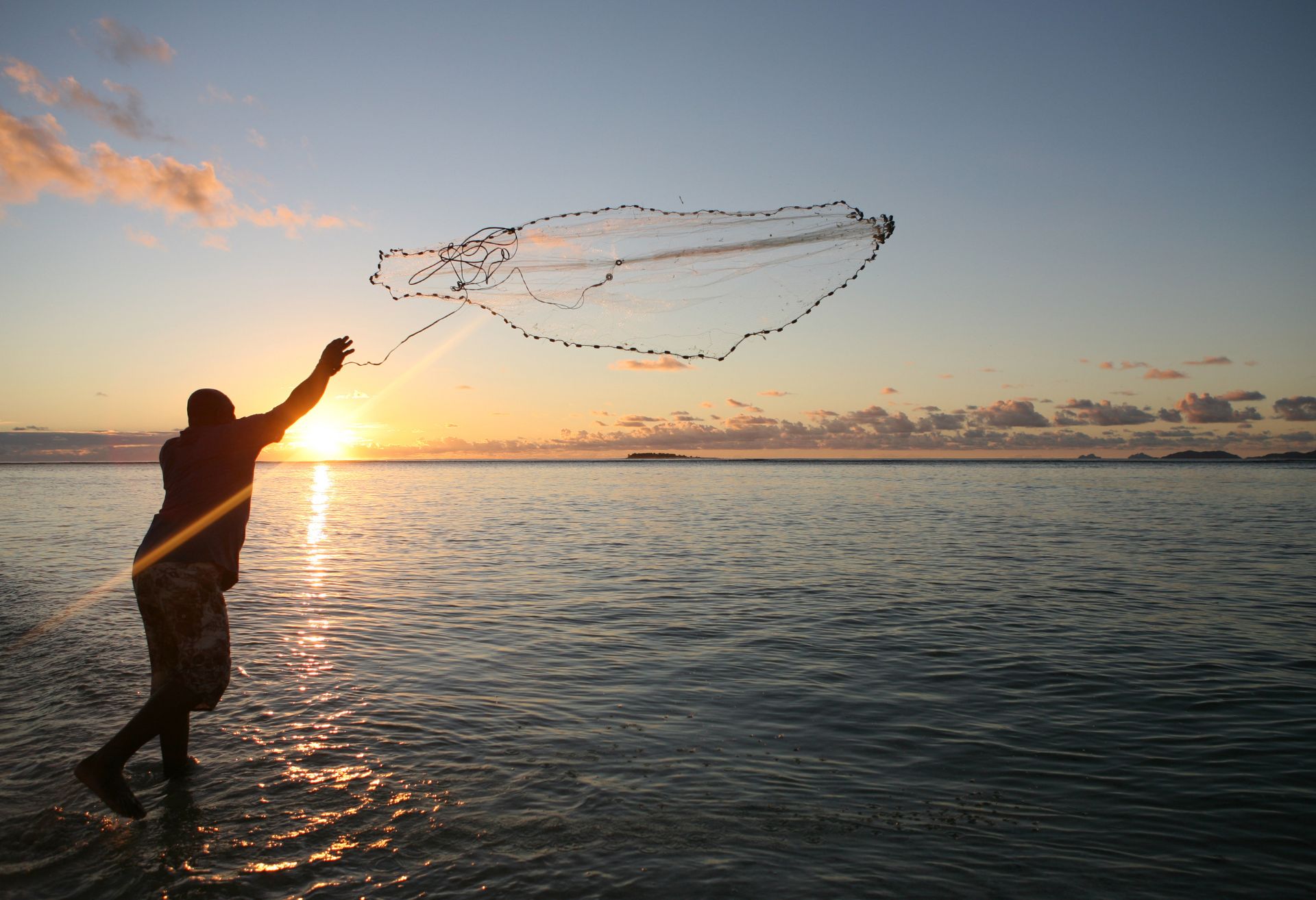 Photograph of a fisherman throwing a net into a lake