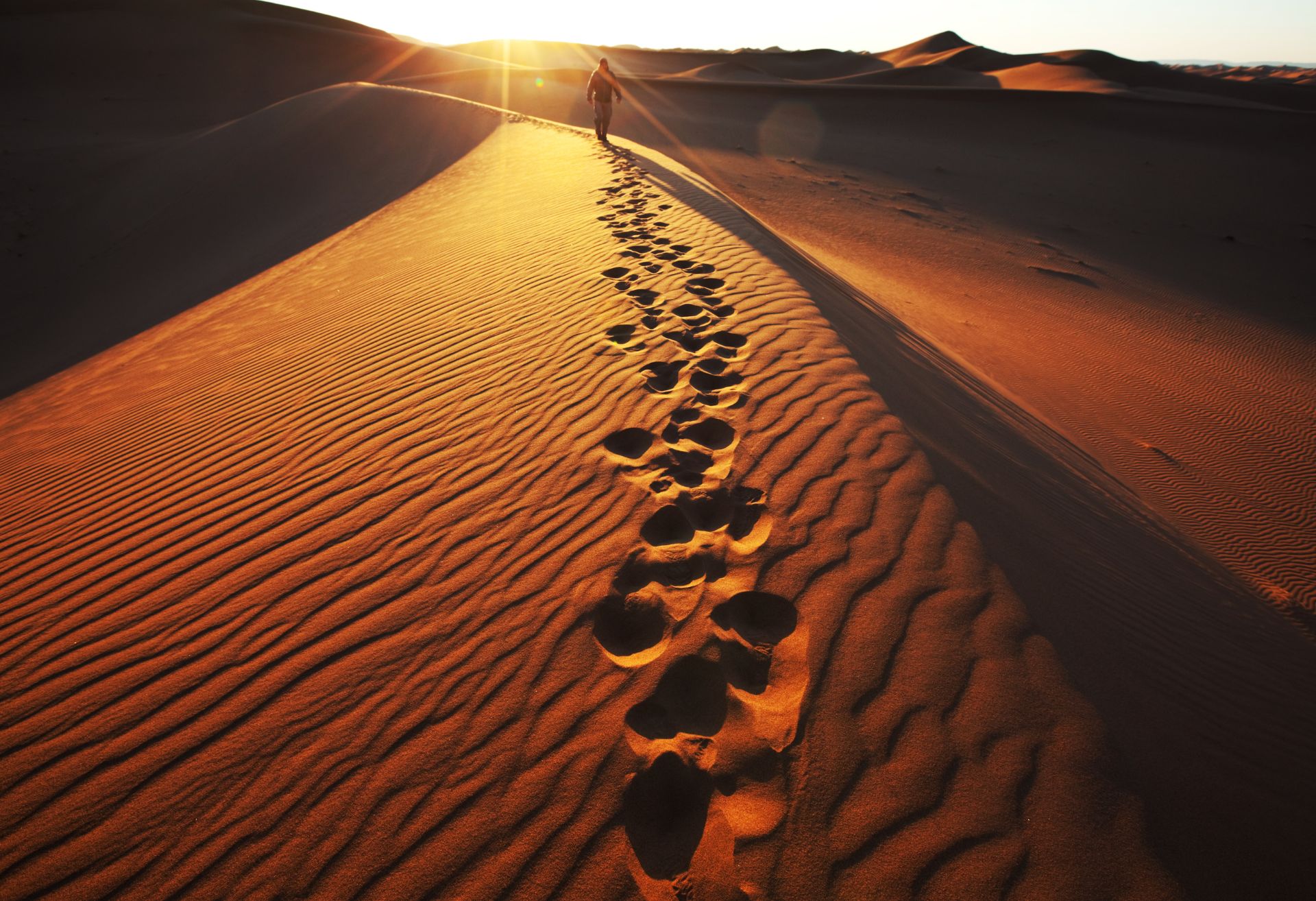 Man walking alone in the desert towards a sunset