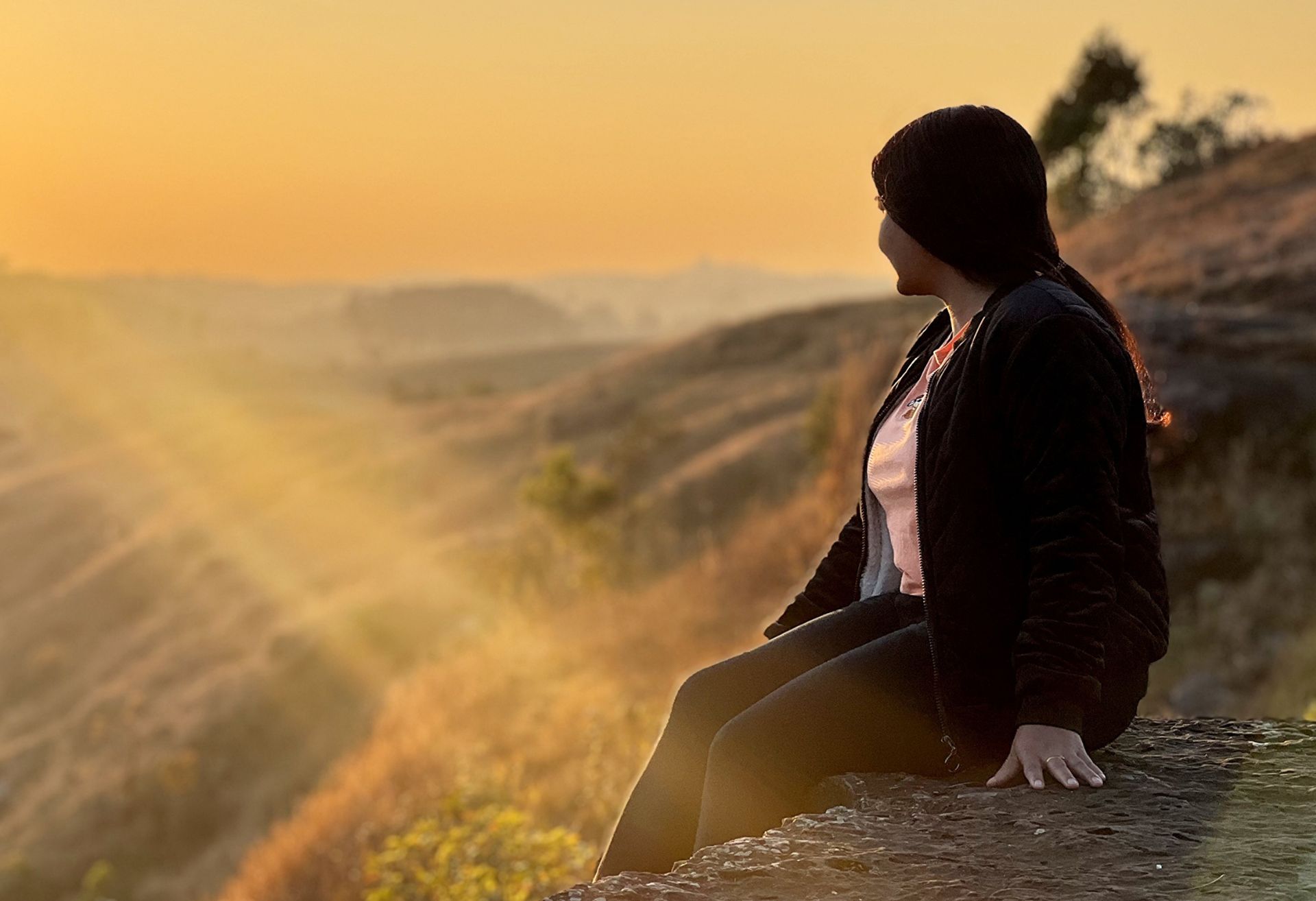 Image of a woman looking at a sunset whilst sat on a hillside